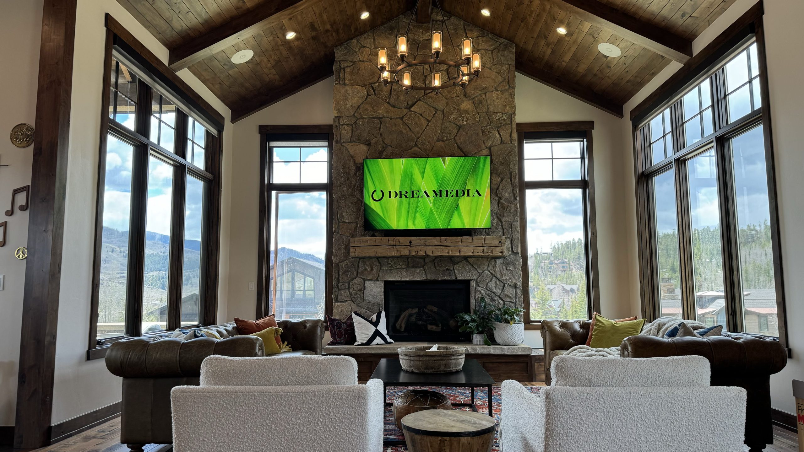 Stylish living room featuring a stone fireplace and large windows, showcasing the Dreamedia logo on a mounted TV.