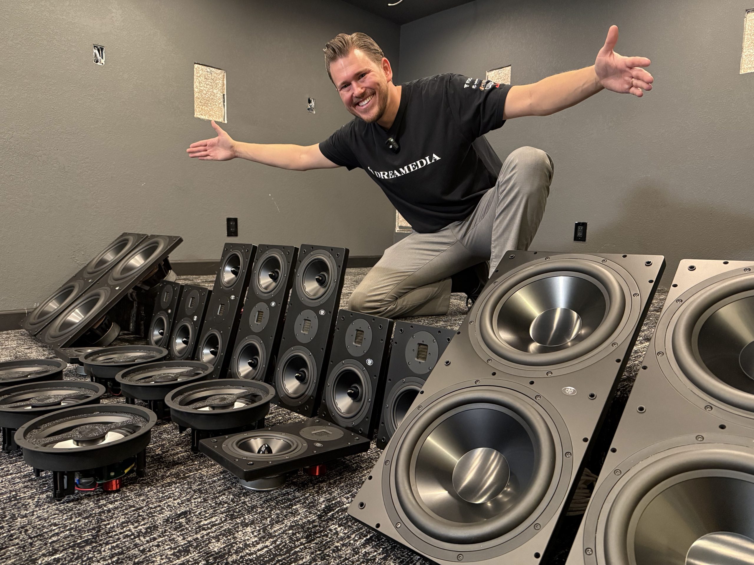 A man showcases a collection of high-quality speakers in a home theater setup, emphasizing audio excellence.
