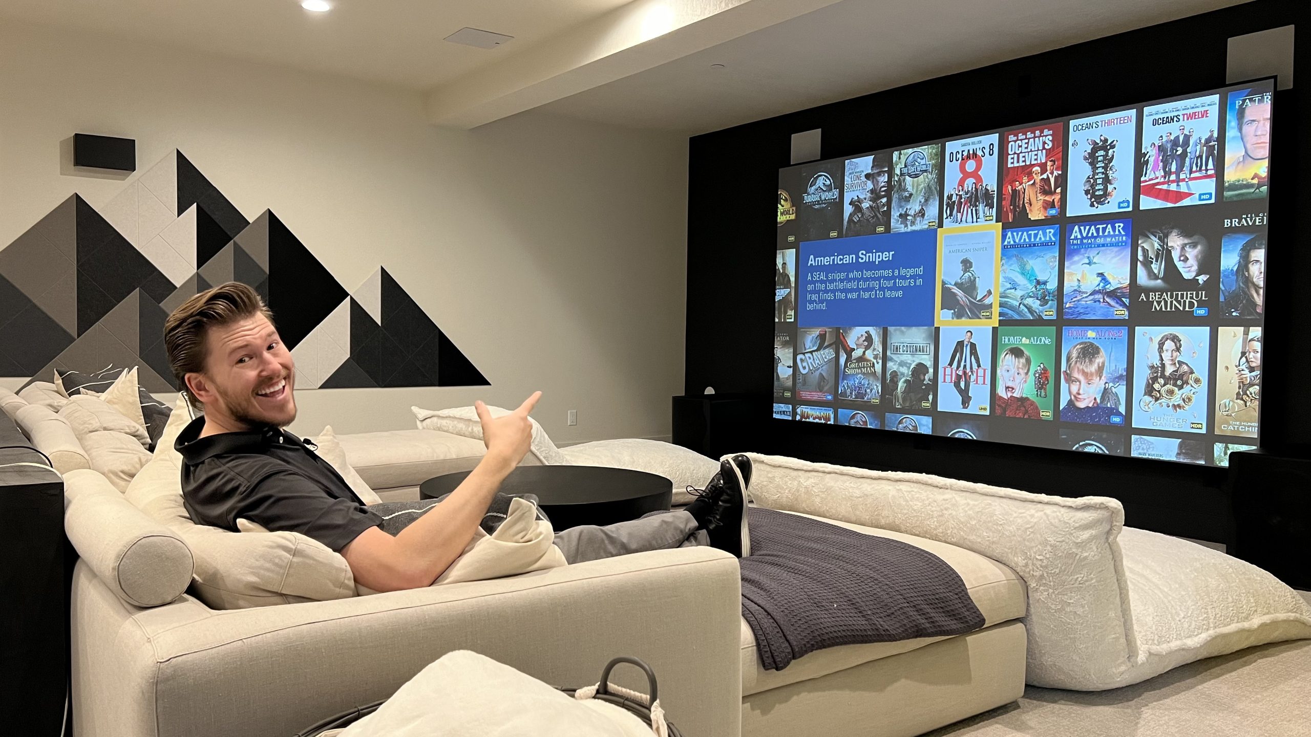 A person enjoys a movie in a stylish home theater, featuring a large projected screen and comfortable seating.