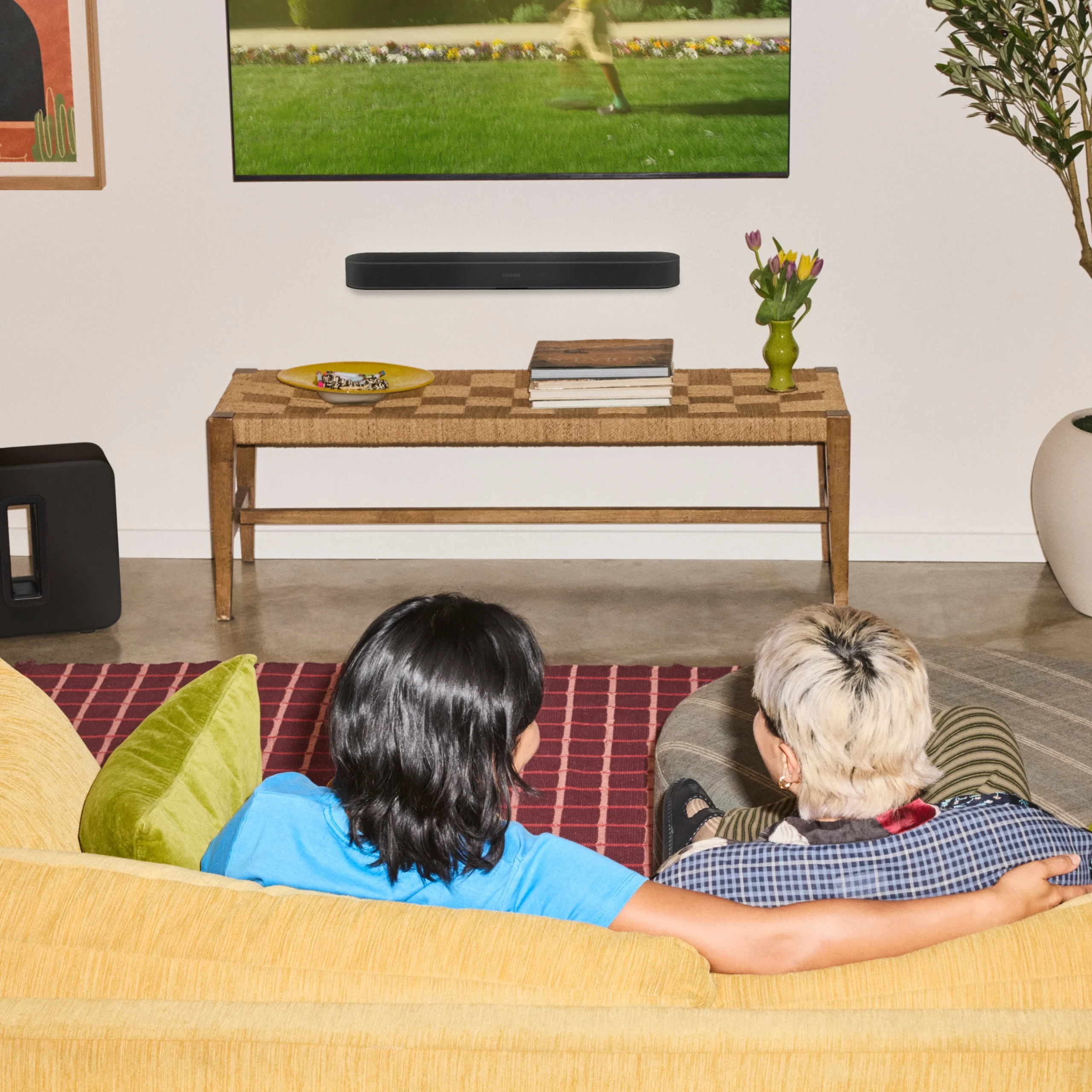 Two friends relax on a couch watching a movie in a stylish home theater, with a soundbar and coffee table in view.