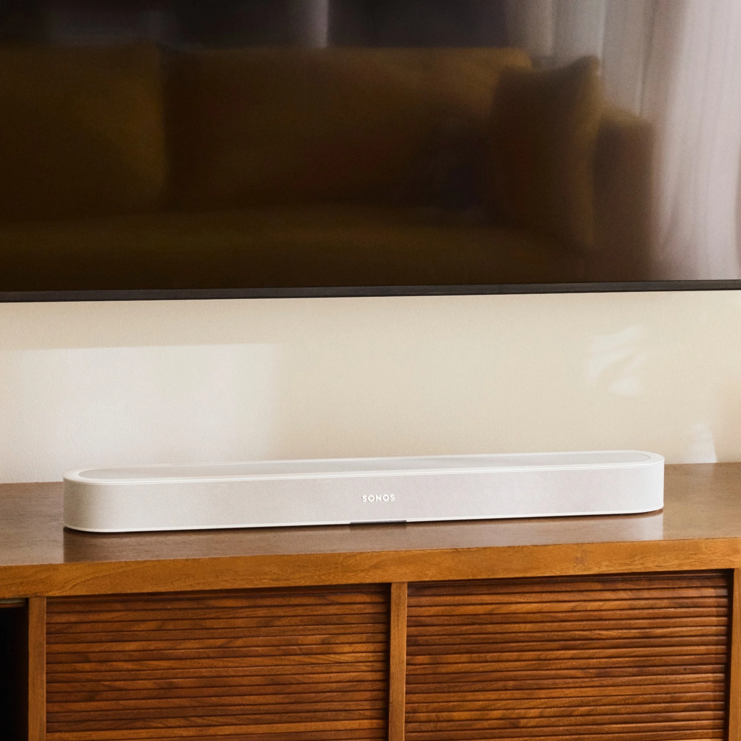 White Sonos soundbar positioned on a wooden cabinet beneath a modern television in a cozy home setting.