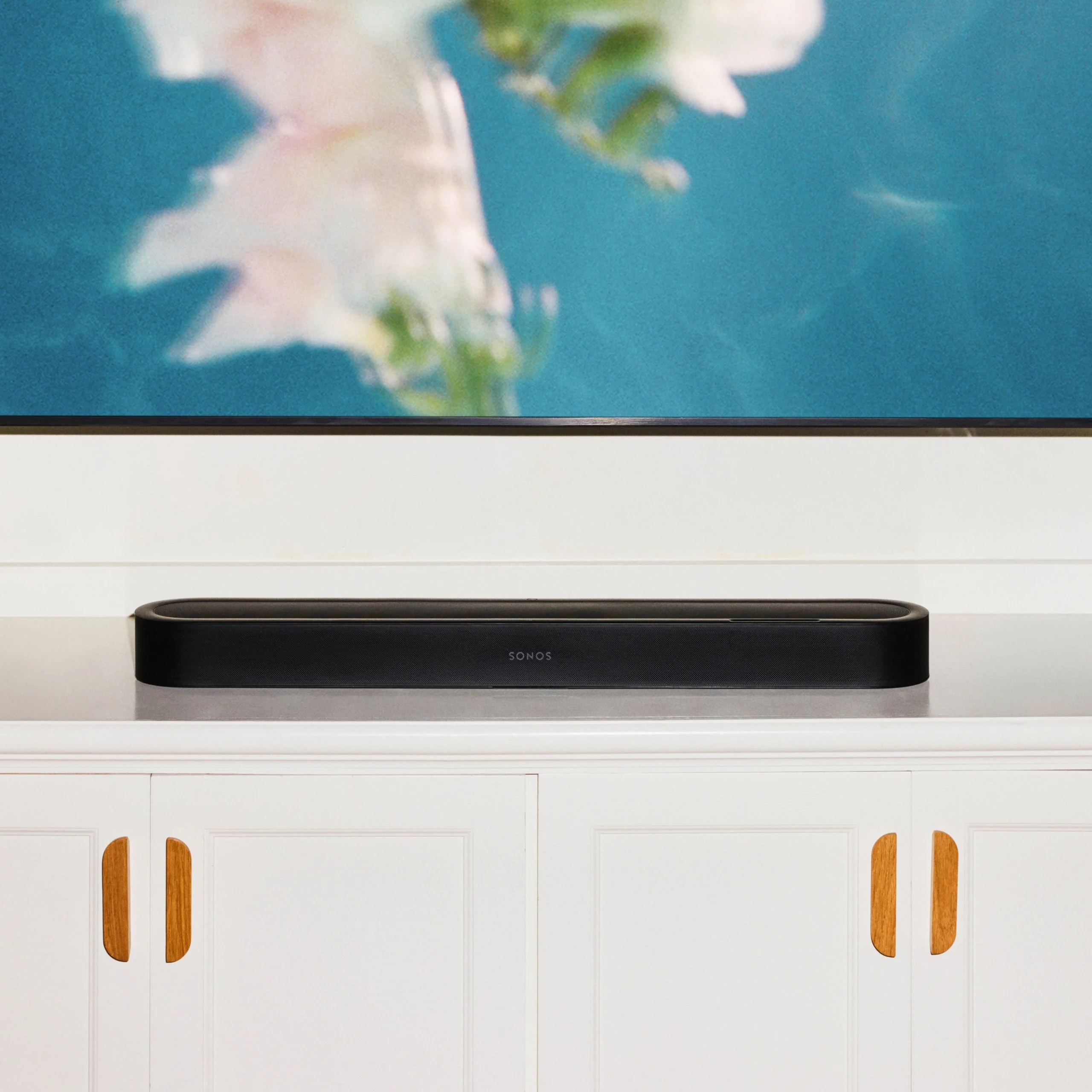 Sonos soundbar positioned sleekly on a white cabinet under a television displaying abstract art.