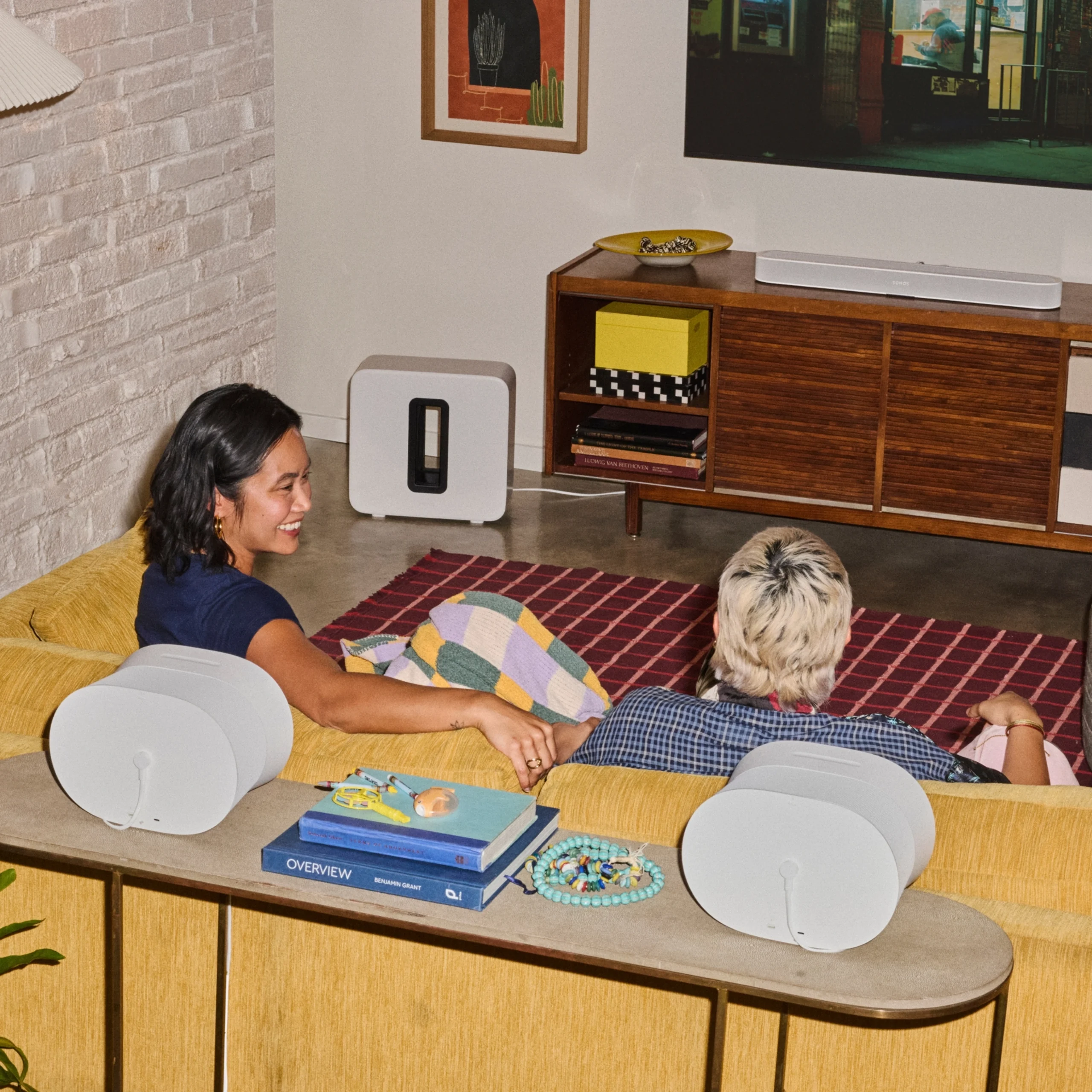 Two friends relax on a cozy yellow sofa, enjoying a movie with stylish audio equipment in a modern home theater setup.