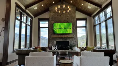Stylish living room featuring a stone fireplace and large windows, showcasing the Dreamedia logo on a mounted TV.