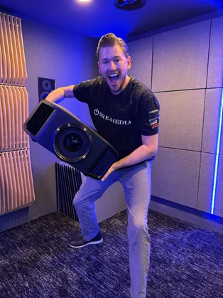 A person in a Dreamedia shirt excitedly displays a high-quality projector in a stylish home theater setup.