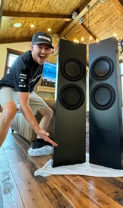 Enthusiastic person showcasing high-end speakers in a stylish home setting, highlighting modern audio design.