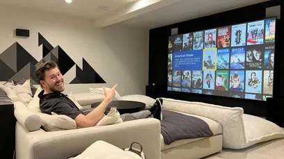 A person enjoys a movie in a stylish home theater, featuring a large projected screen and comfortable seating.