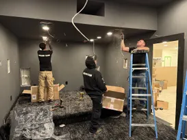 Workers from Dreamedia install lighting and wiring in a luxury home theater under construction, showcasing their teamwork.