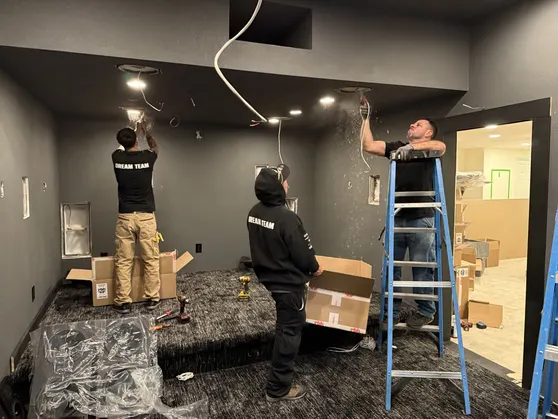 Workers from Dreamedia install lighting and wiring in a luxury home theater under construction, showcasing their teamwork.